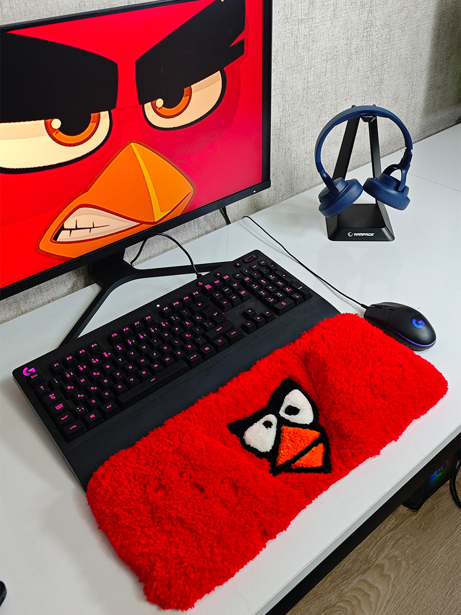 Canlı kırmızı renkte, Angry Birds karakterinin göz ve gaga detaylarıyla işlenmiş, yumuşak tüylü dokuya sahip el yapımı tufting klavye pedi ve masaüstü konforu sağlayan gaming tufting halısı.