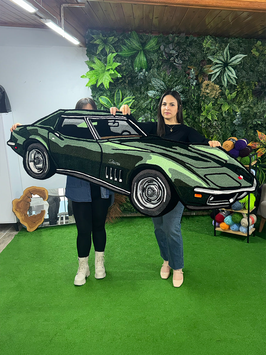 İki kişi tarafından havada tutulan, gerçekçi boyutları ve klasik otomobil hatlarını vurgulayan yeşil renkli özel tasarım Corvette tufting halı.