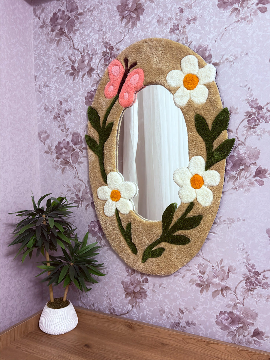 Çiçekli duvar kağıdı önünde sergilenen, bej zemin üzerine beyaz papatya ve pembe kelebek nakışlı Floren el yapımı tufting duvar halısı çerçeveli ayna.