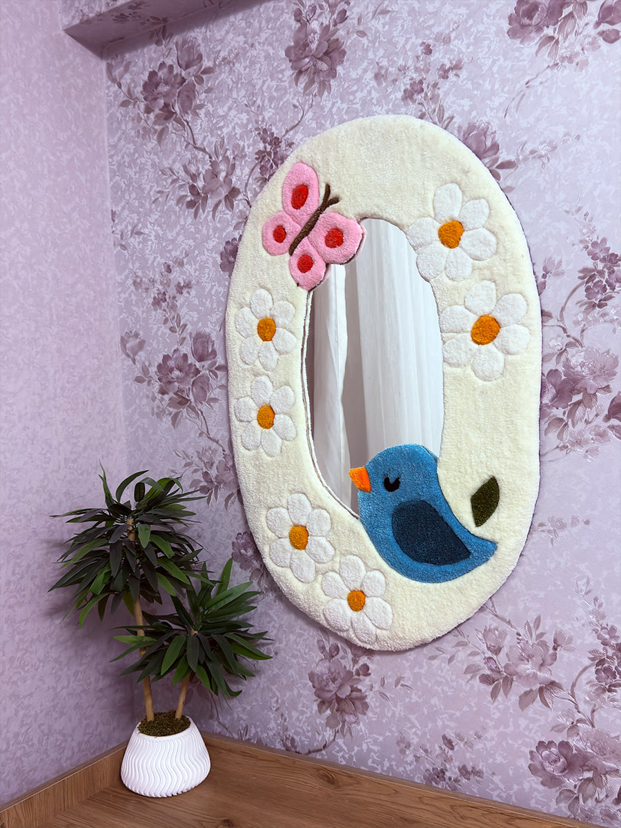 Duvara asılı konumda sergilenen, açık renkli yumuşak çerçevesi ve masalsı tasarımıyla mekanlara sıcak bir atmosfer katan pastoral temalı el yapımı tufting halı ayna.