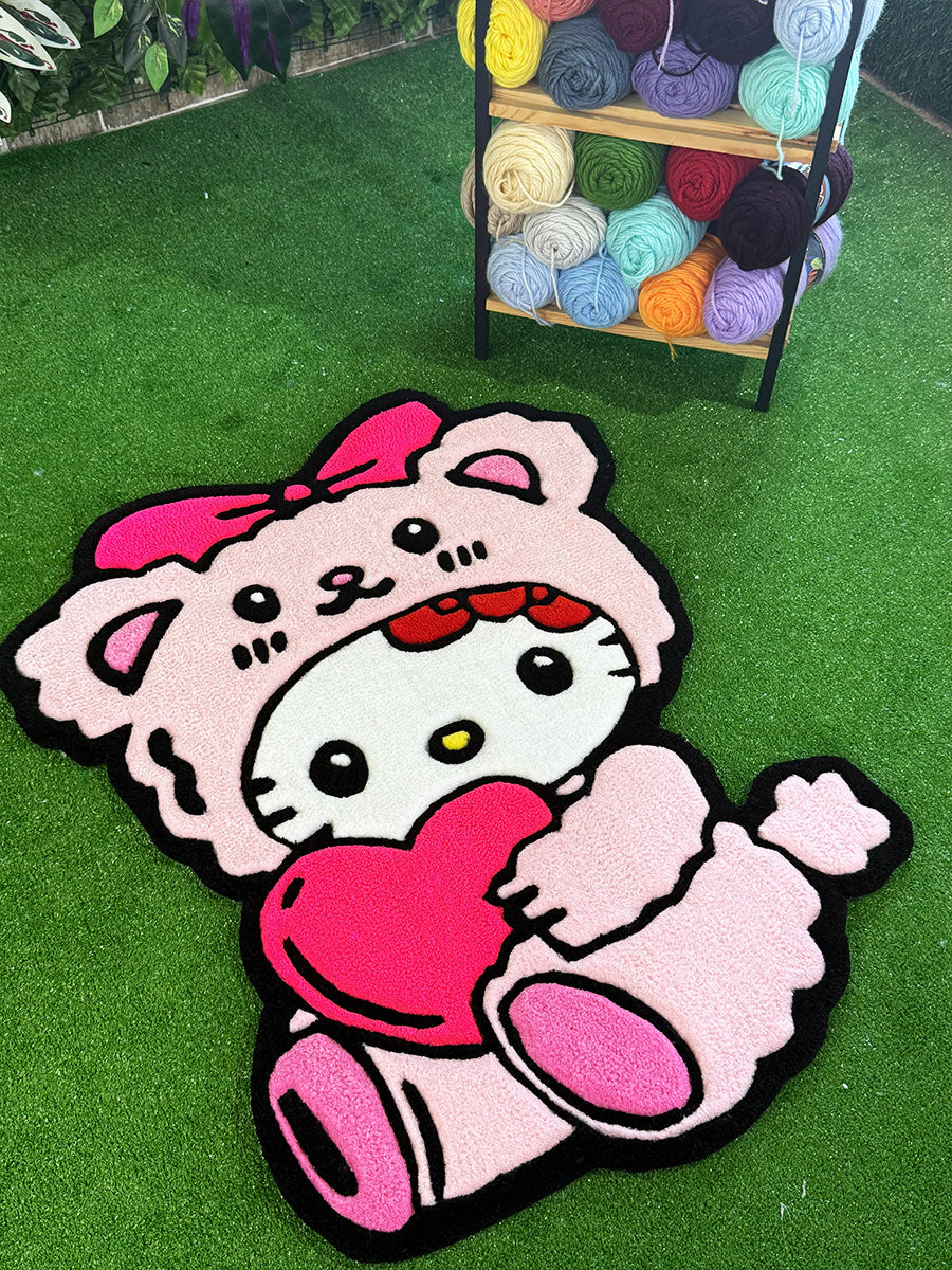 Pembe ayıcık kostümü giymiş ve pembe bir kalp tutan sevimli Hello Kitty Pink Edition el yapımı tufting halının çapraz açıdan çekilmiş dekoratif görünümü.