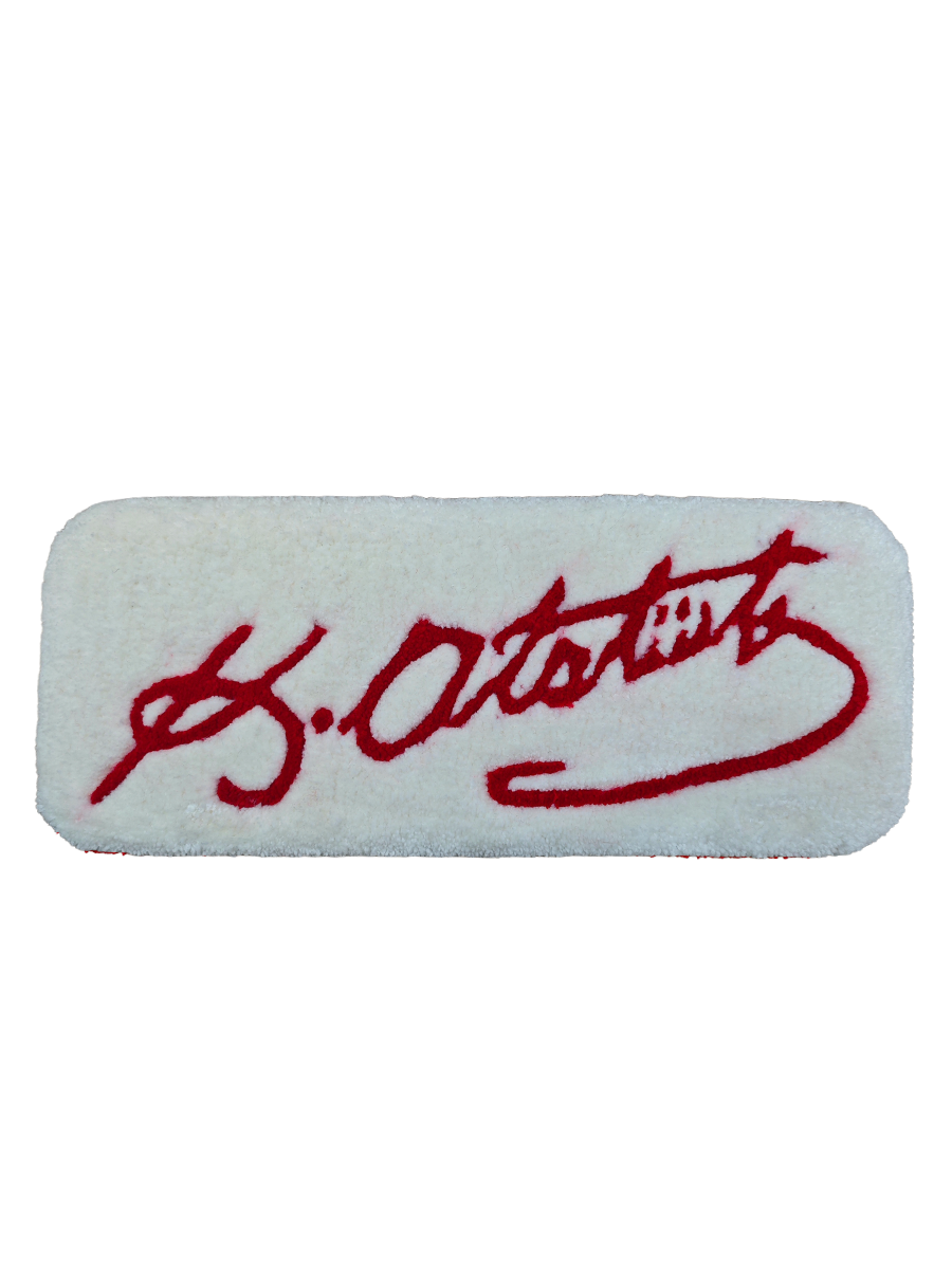 Beyaz zemin üzerine canlı kırmızı iplikle işlenmiş K. Atatürk imzalı el yapımı tufting klavye pedi, 42x17 cm boyutlarındaki yüksek havlı ve yumuşak dokusuyla çalışma masalarına hem ergonomik bir bilek desteği hem de estetik bir değer katıyor.