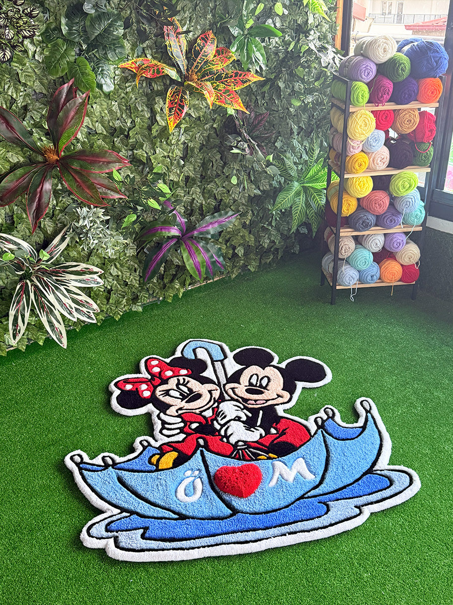Birinci sınıf akrilik iplerle dokunmuş, şemsiye içinde oturan sevimli Mickey ve Minnie Mouse figürlü el yapımı dekoratif halı. GG Tufting kalitesini yansıtan, kalın havlı yapısı ve zemindeki duruşuyla öne çıkan canlı renklere sahip tufting çocuk odası halısı.