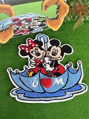 Mavi bir şemsiye altında neşeyle birbirine sarılan Mickey ve Minnie Mouse figürlerinin işlendiği, kırmızı kalp detaylı el yapımı tufting halı. Canlı renklere ve yumuşak dokuya sahip bu dekoratif çocuk odası halısı modelinin, detayları öne çıkaran yakından çekilmiş açılı görünümü.