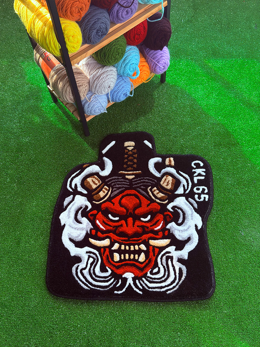 Üst köşesinde CKL 65 yazısı bulunan, kahverengi boynuzlar ve tepesindeki kılıç kabzası figürleriyle siyah zemin üzerine tasarlanmış JDM temalı tufting halı el yapımı araç paspası.