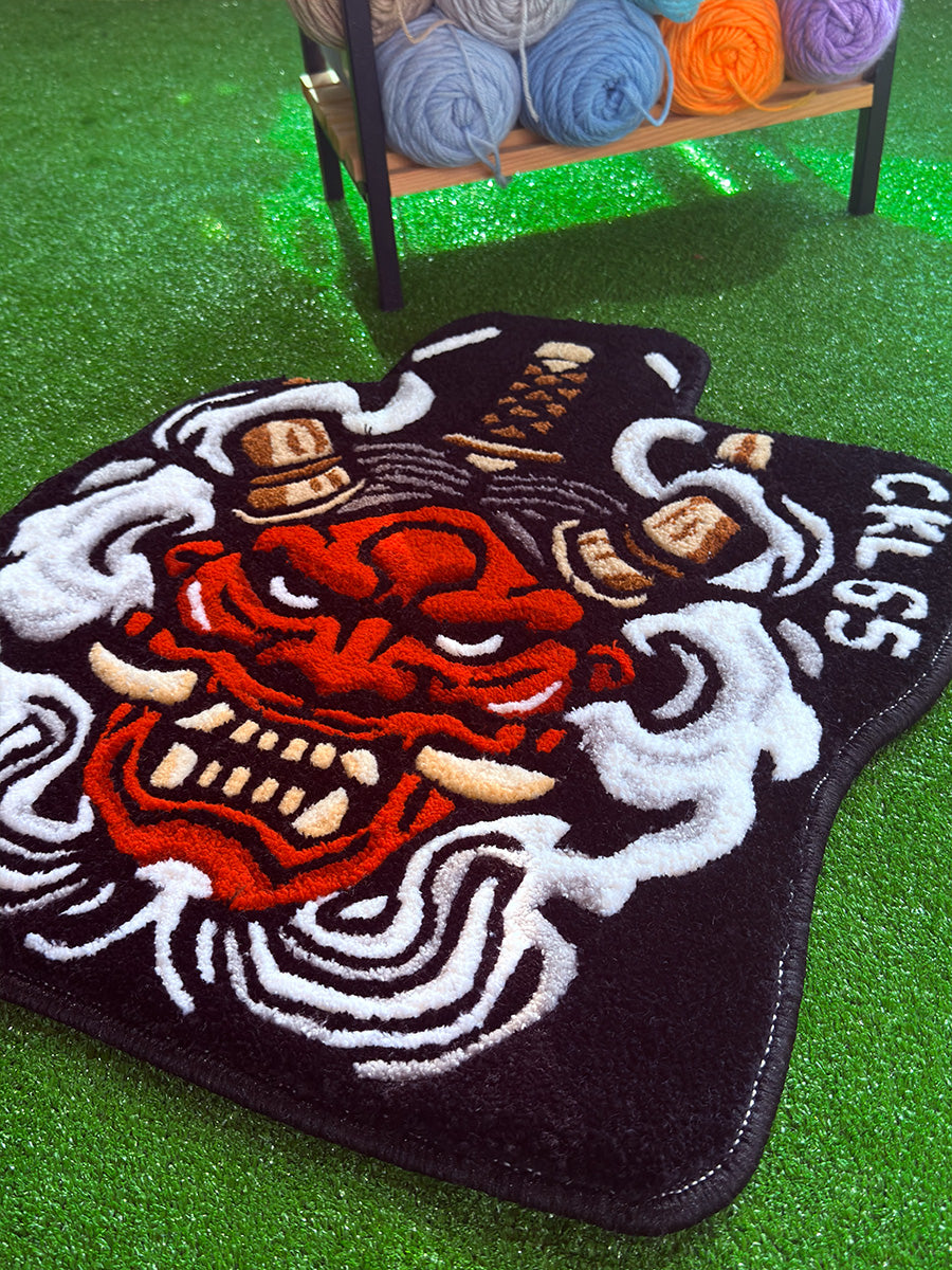 Siyah zemin üzerine kırmızı Oni maskesi ve beyaz duman motifleriyle işlenmiş, 3D traşlama tekniğiyle derinlik kazandırılmış el yapımı tufting halı araç paspası tasarımı.