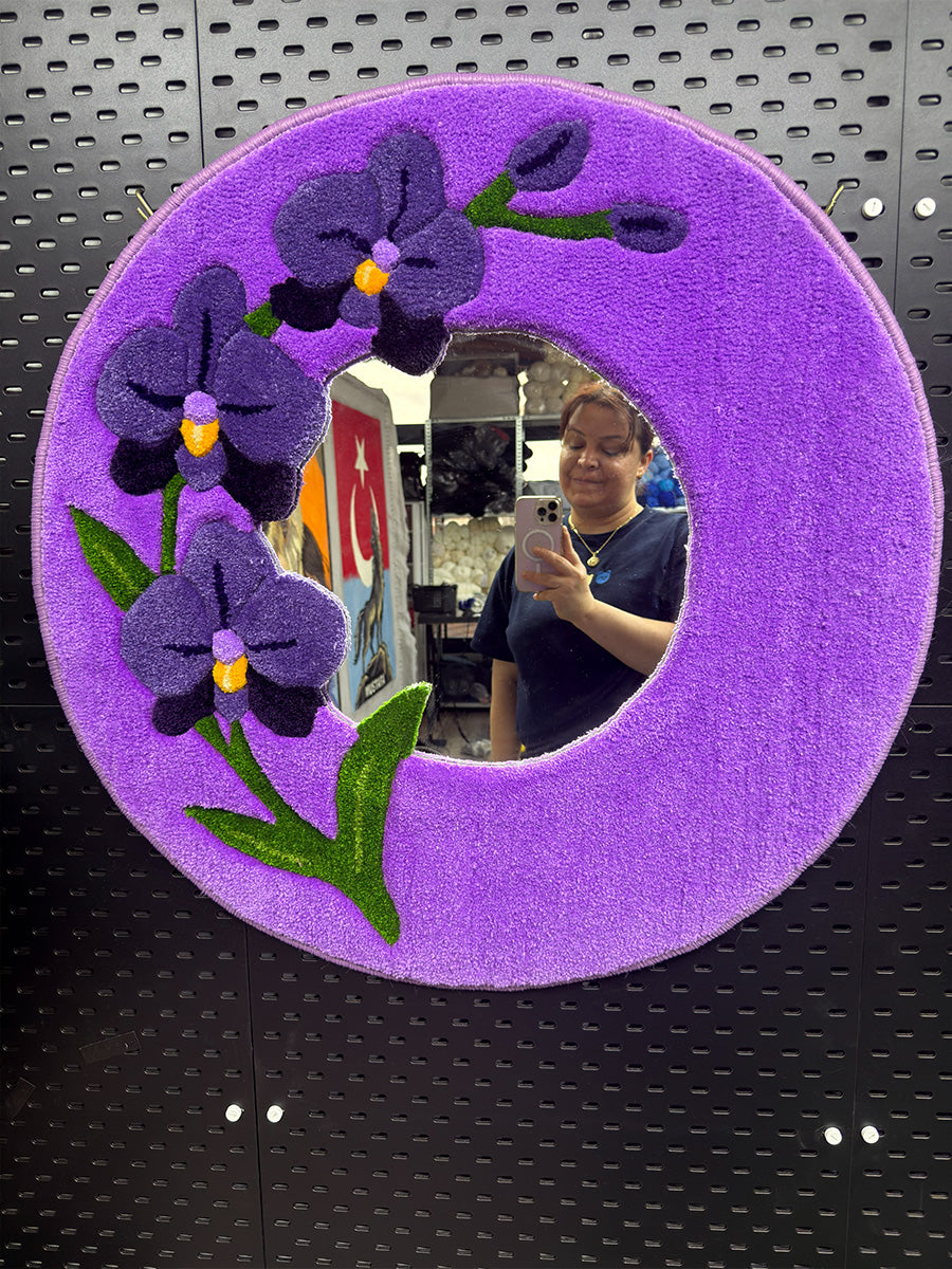 Mor orkide desenli el yapımı dekoratif tufting ayna; dairesel formdaki aynanın yansıma detayını ve çerçeve dokusunu gösteren ön plan çekimi.