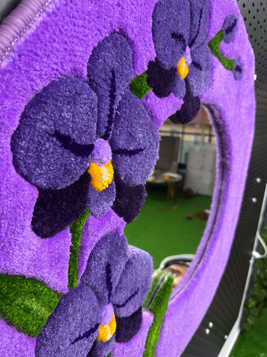 Tufting tekniği ile hazırlanan mor orkide aynanın üst açıdan yakın çekimi; el tıraşlaması (carving) ile belirginleştirilmiş çiçek desenleri ve yumuşak dokusu.