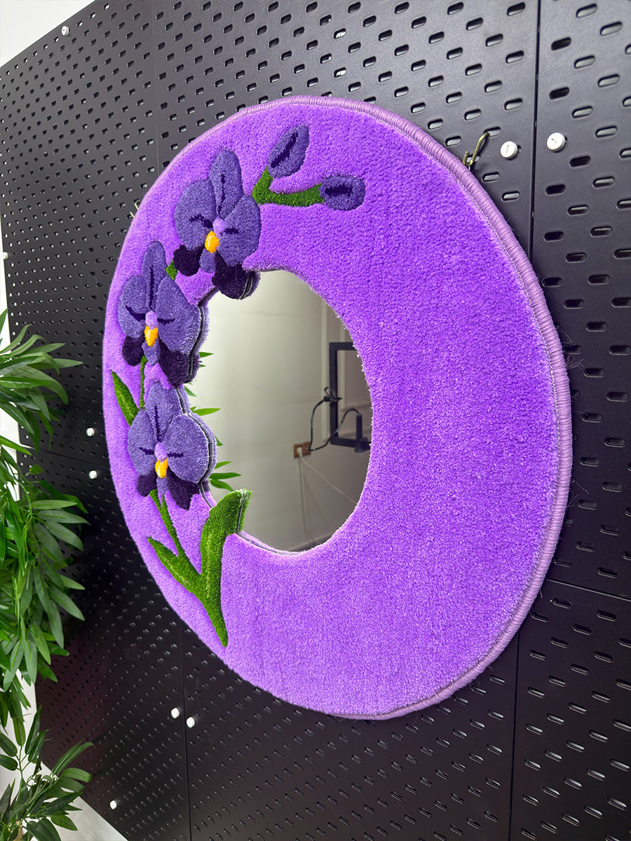 Siyah dekoratif panel üzerinde sergilenen dairesel formdaki mor orkide desenli tufting duvar aynası, modern tasarımı ve canlı akrilik iplik renkleriyle estetik bir duruş sergiliyor.