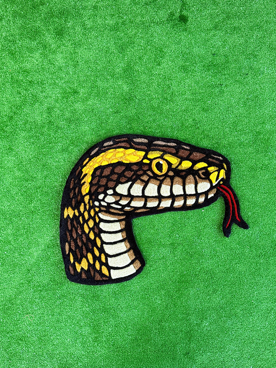 Üstten çekimle yılan başı formunun tam olarak sergilendiği, 75x57 cm ölçülerindeki HYDRA el yapımı halı. Kahverengi tonlarındaki güçlü yırtıcı deseni ve kalın dokusuyla dikkat çeken hayvan figürlü egzotik tufting halı tasarımı.
